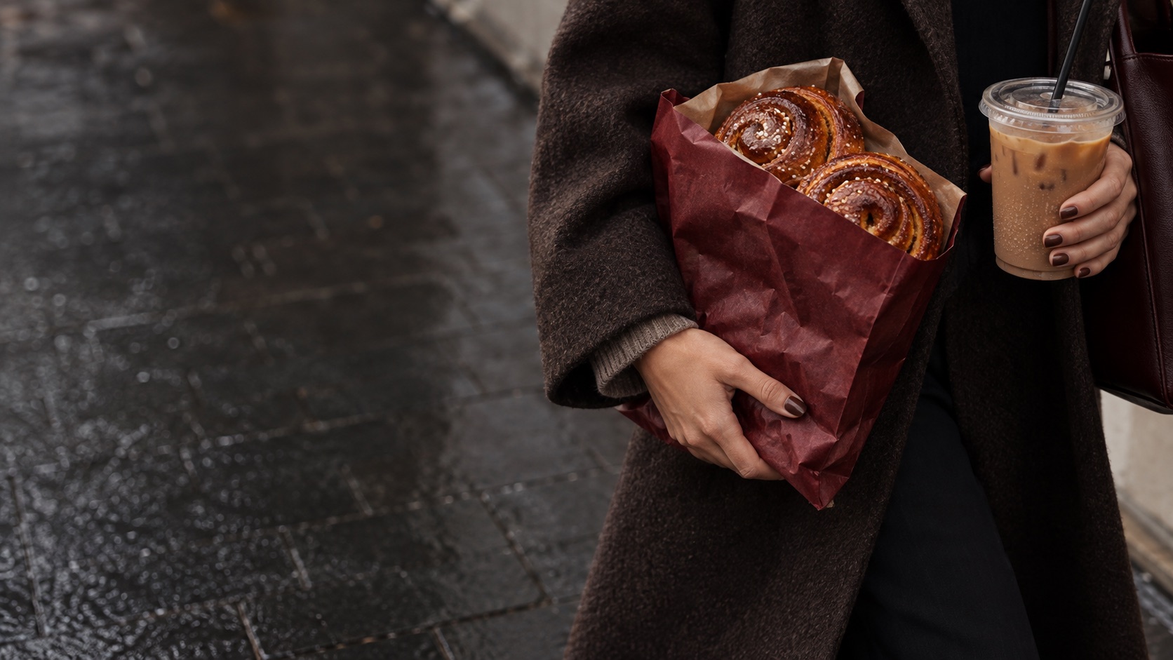 Cinnamon buns in a burgundy bakery bag with an iced coffee